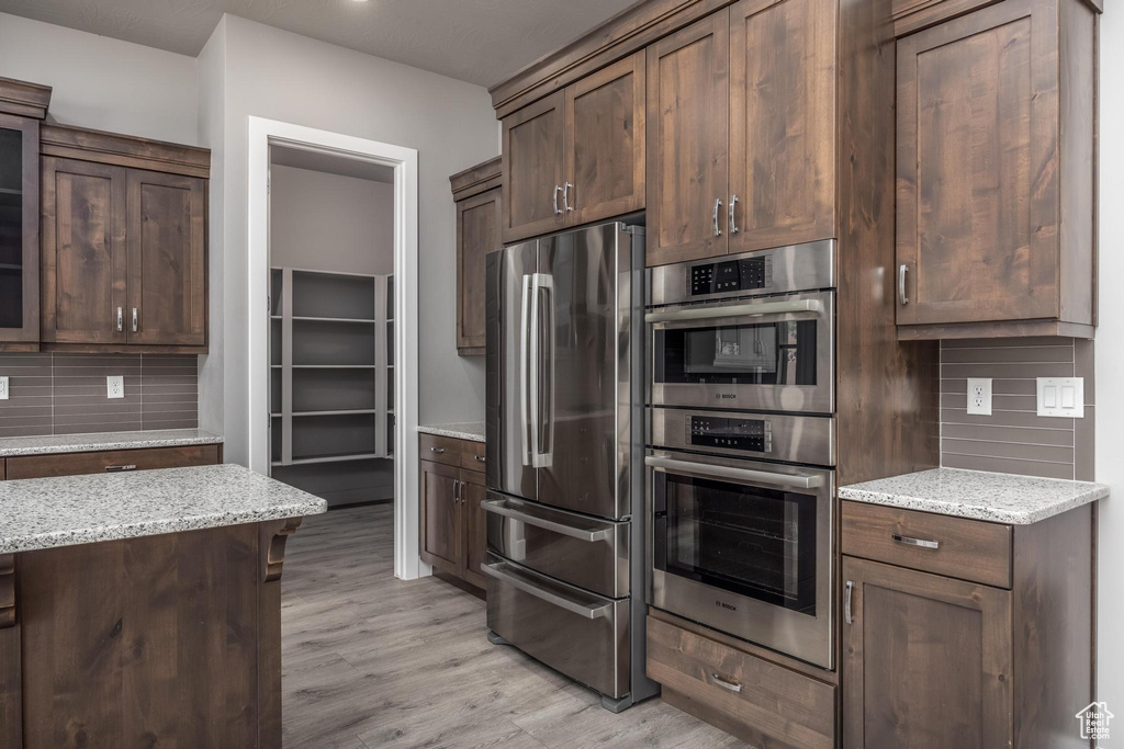 Kitchen featuring appliances with stainless steel finishes, light wood-style floors, light stone counters, and decorative backsplash