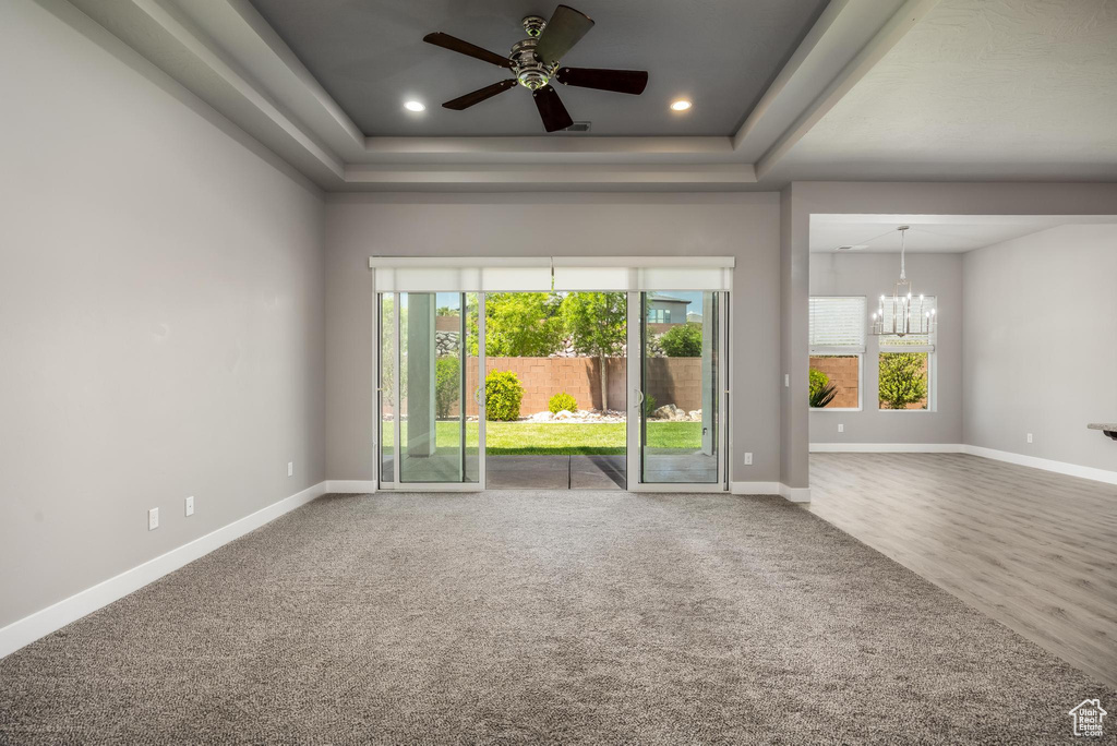 Carpeted spare room with a chandelier, a ceiling fan, baseboards, a raised ceiling, and recessed lighting