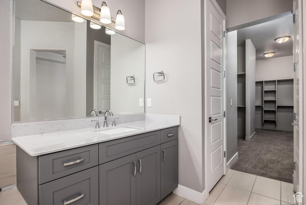 Bathroom featuring vanity, baseboards, a walk in closet, and tile patterned floors