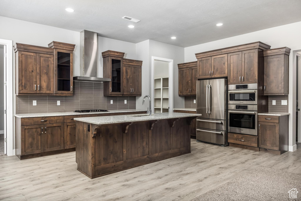 Kitchen featuring appliances with stainless steel finishes, wall chimney exhaust hood, decorative backsplash, a breakfast bar, and recessed lighting