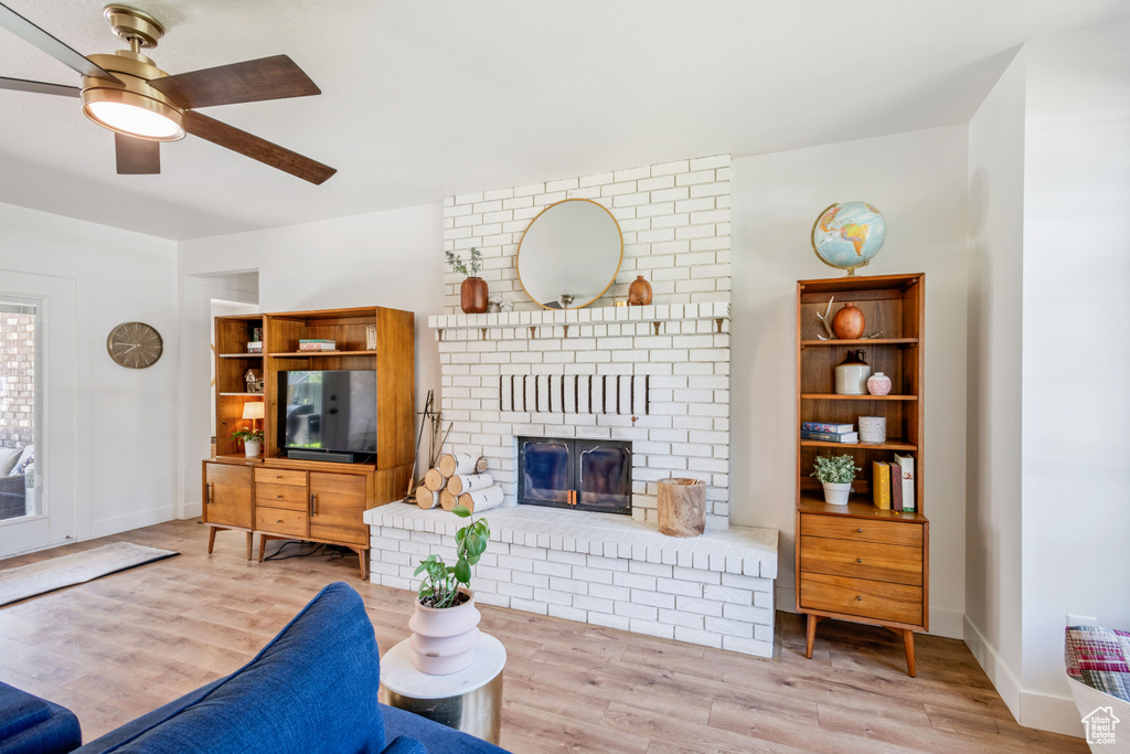 Living area with wood finished floors, a ceiling fan, a brick fireplace, and baseboards
