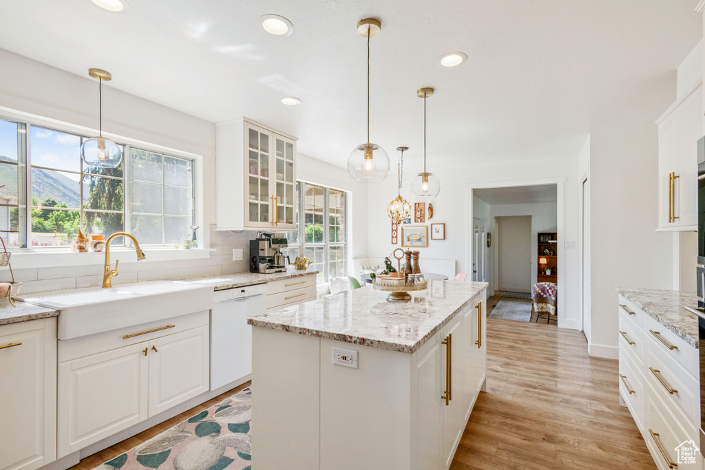 Kitchen with white dishwasher, glass insert cabinets, light wood finished floors, a center island, and white cabinets