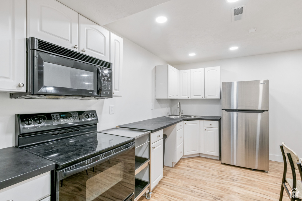 Kitchen with black appliances, a sink, white cabinets, light wood finished floors, and recessed lighting