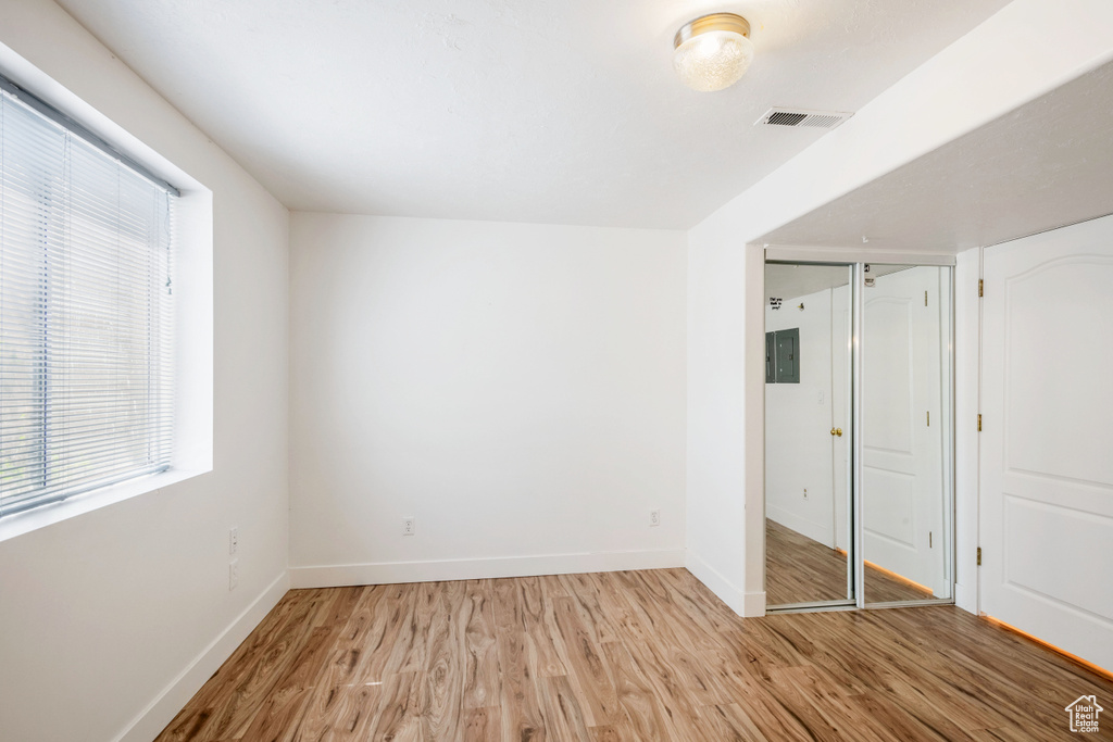 Unfurnished bedroom featuring light wood-style flooring, baseboards, multiple windows, and electric panel
