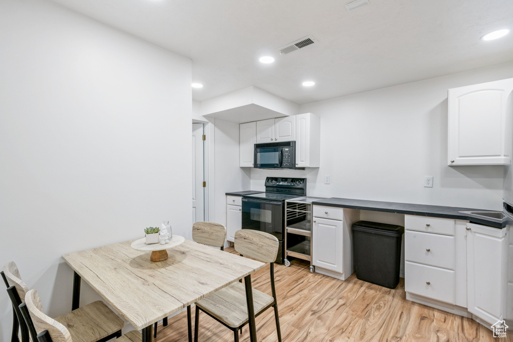Kitchen featuring black appliances, white cabinetry, dark countertops, light wood-style flooring, and recessed lighting