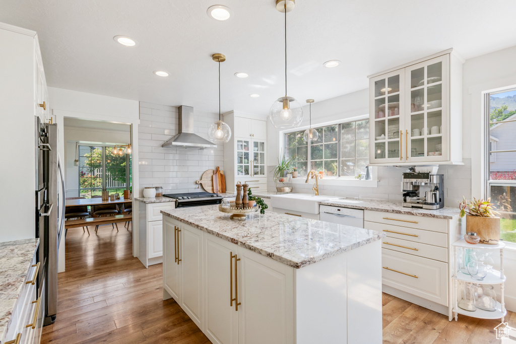 Kitchen with wall chimney exhaust hood, a sink, tasteful backsplash, glass insert cabinets, and recessed lighting