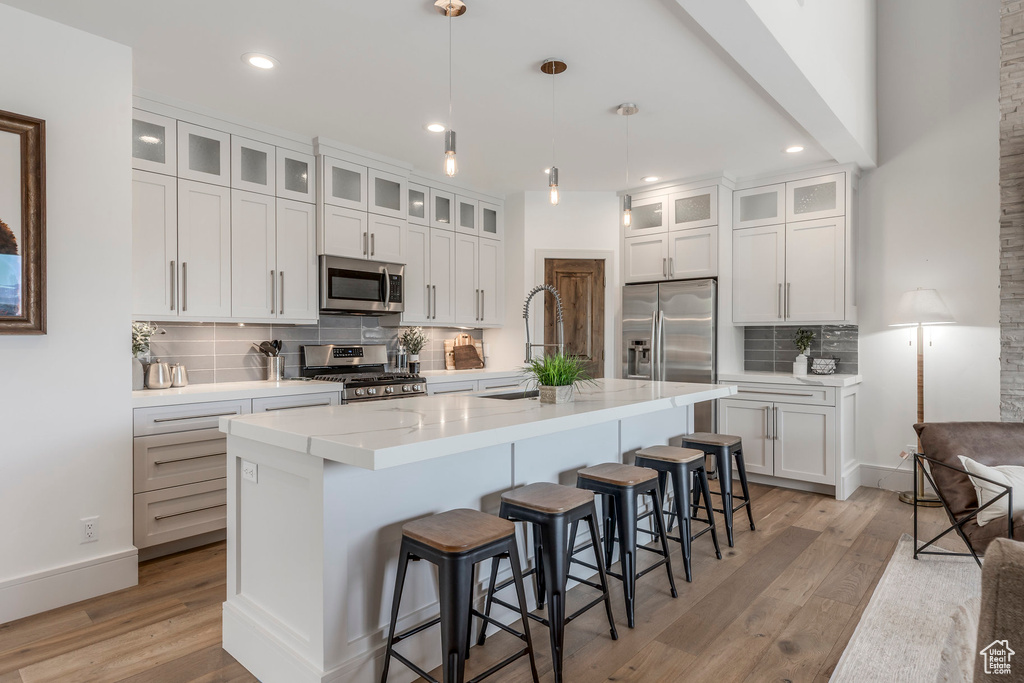 Kitchen featuring appliances with stainless steel finishes, decorative backsplash, light wood finished floors, a sink, and recessed lighting