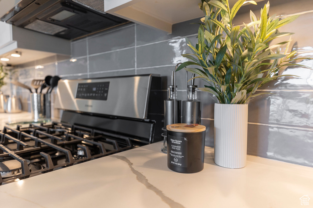 Kitchen view of stainless steel gas stove, decorative backsplash, and range hood
