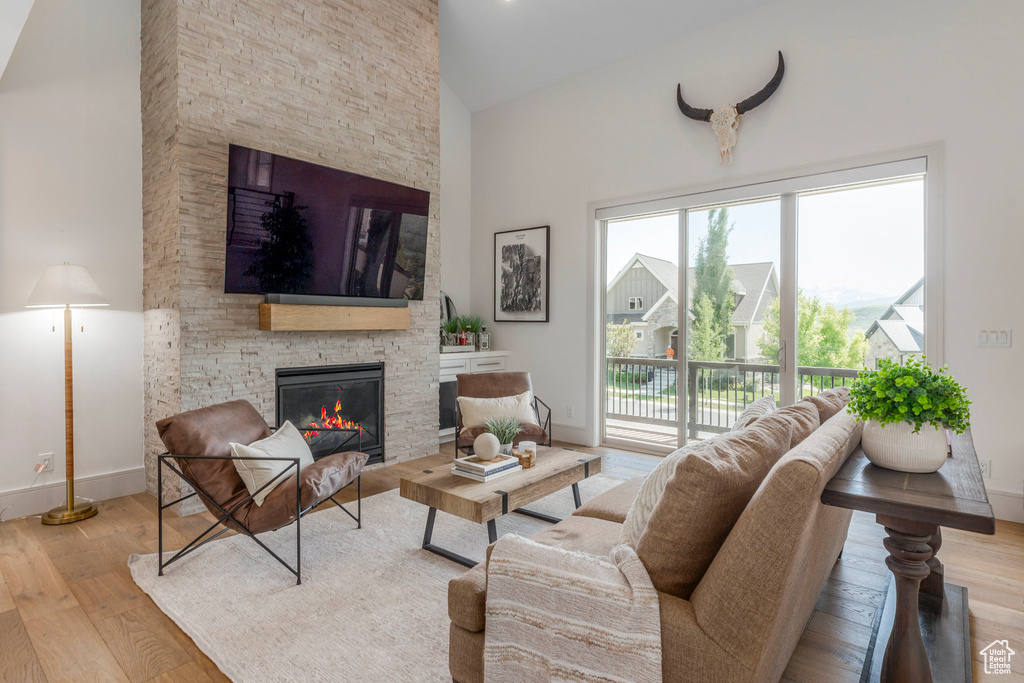 Living area with a stone fireplace, baseboards, wood finished floors, and high vaulted ceiling