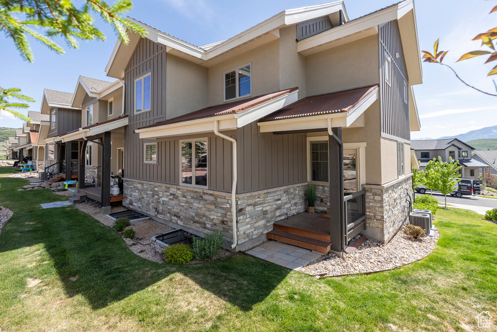 View of front of house with stone siding, a front yard, central AC unit, and board and batten siding