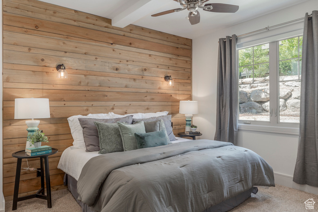 Carpeted bedroom with wooden walls, a ceiling fan, and beam ceiling
