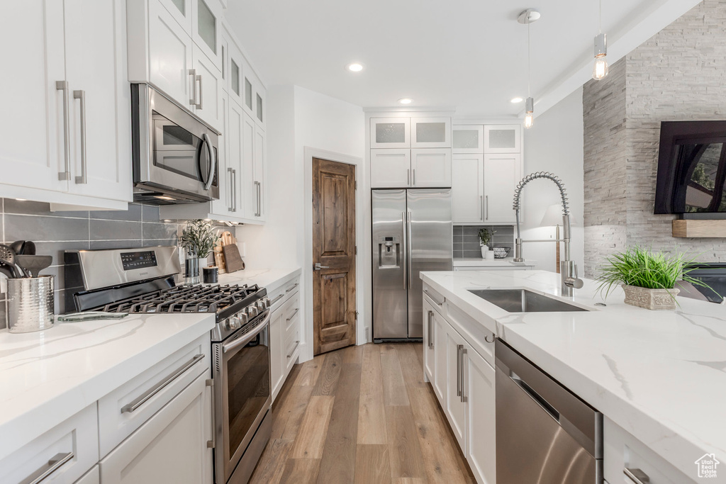 Kitchen featuring stainless steel appliances, a sink, light wood-style flooring, decorative backsplash, and decorative light fixtures