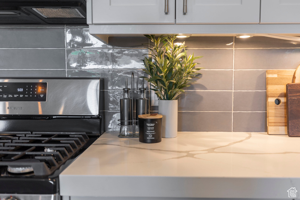 Kitchen view of stainless steel gas stove, backsplash, light stone countertops, and range hood