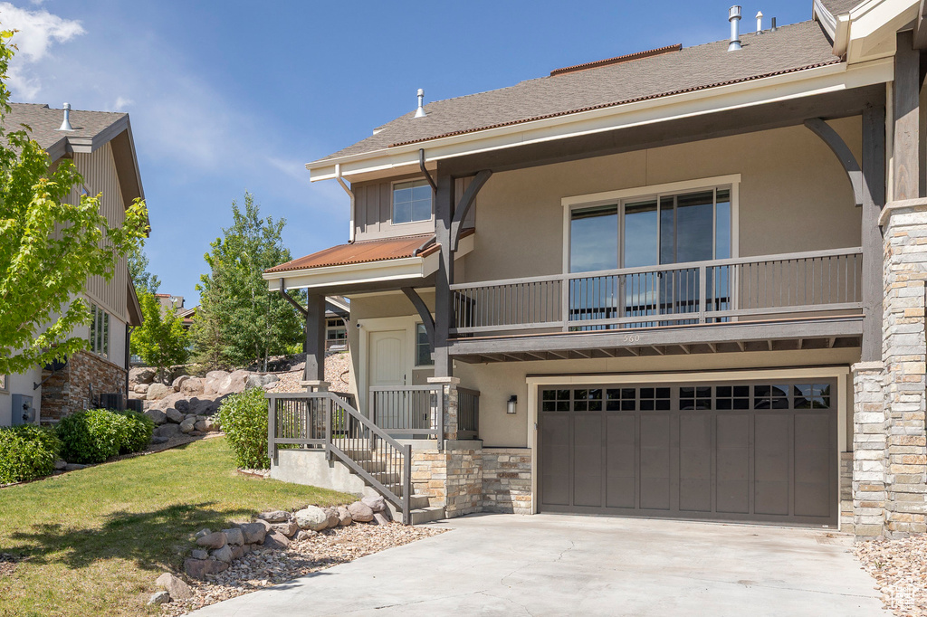 View of front of house featuring stone siding, stucco siding, an attached garage, and a balcony