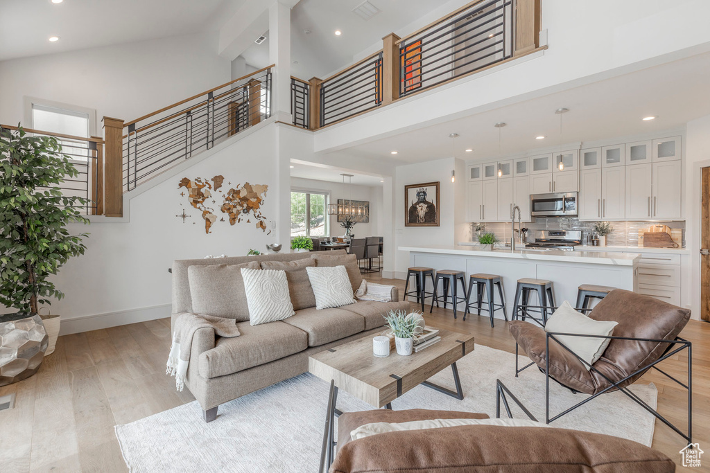 Living area with light wood-type flooring, high vaulted ceiling, baseboards, recessed lighting, and stairs