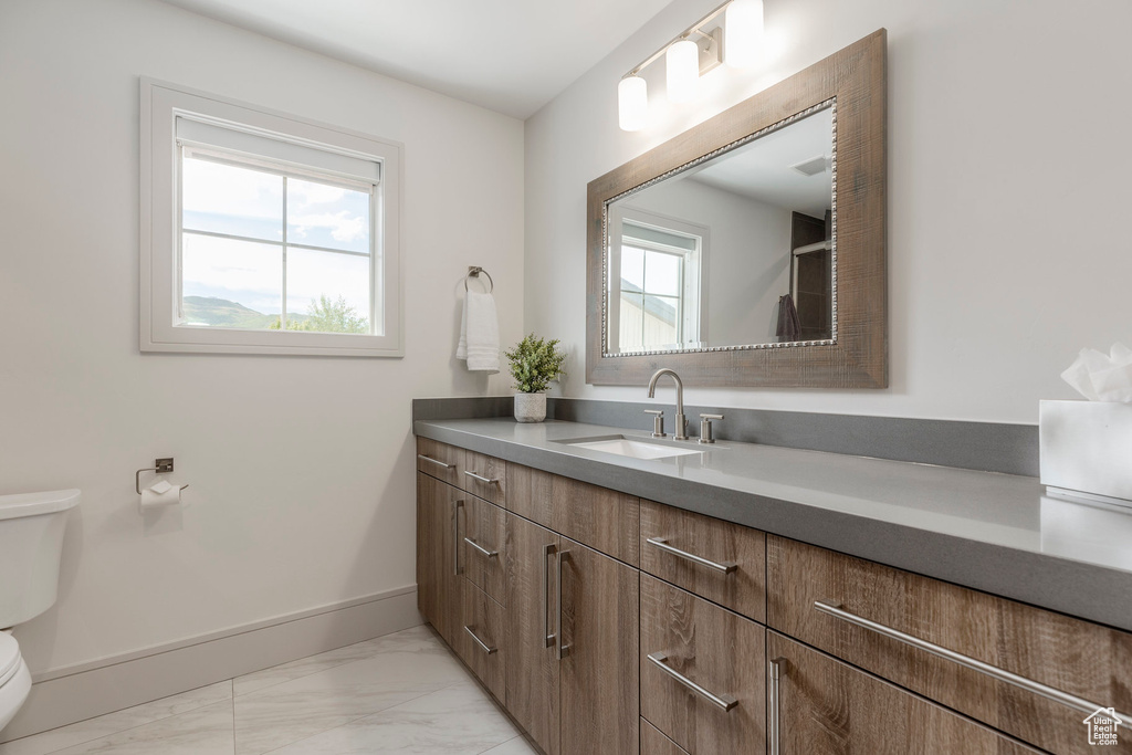 Bathroom with toilet, marble look tiles, vanity, and baseboards
