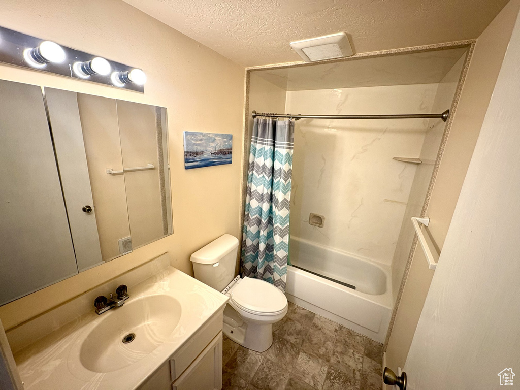 Bathroom with vanity, shower / bathtub combination with curtain, toilet, a textured ceiling, and stone finish floors