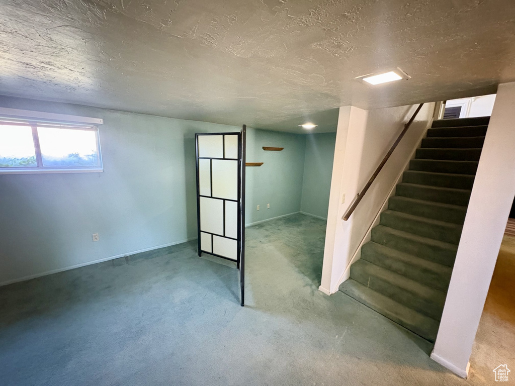 Below grade area featuring a textured ceiling, stairway, carpet, and baseboards