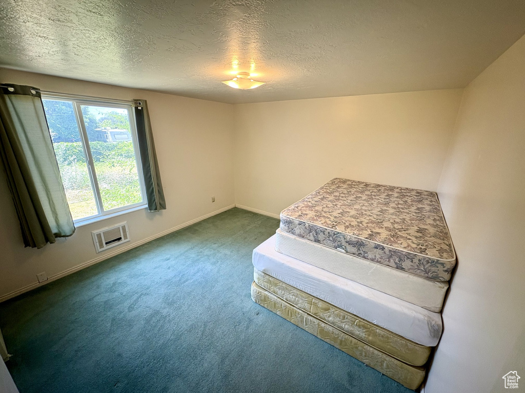 Unfurnished bedroom featuring dark carpet, baseboards, and a textured ceiling