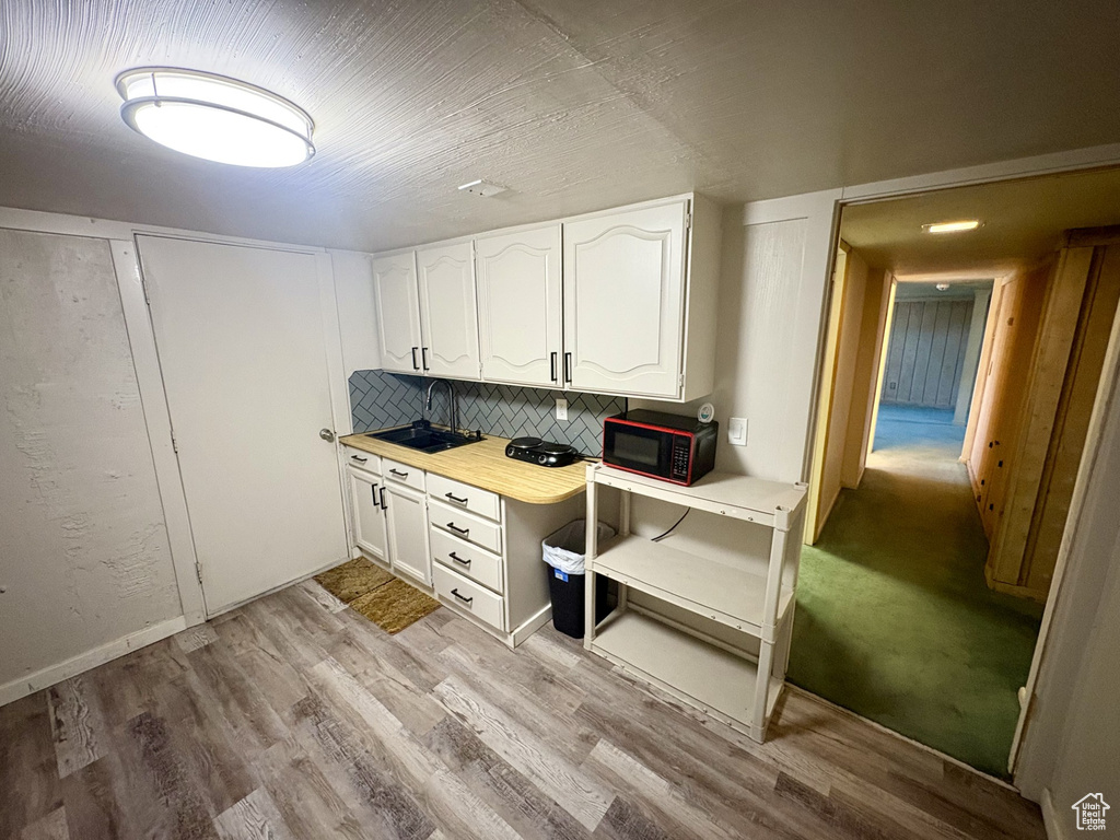 Kitchen with black microwave, white cabinets, a sink, light wood-style flooring, and tasteful backsplash