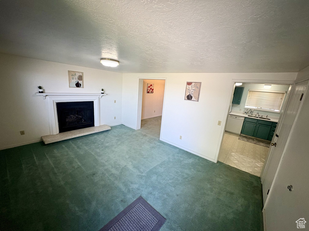 Unfurnished living room with carpet, a fireplace with raised hearth, baseboards, a sink, and a textured ceiling