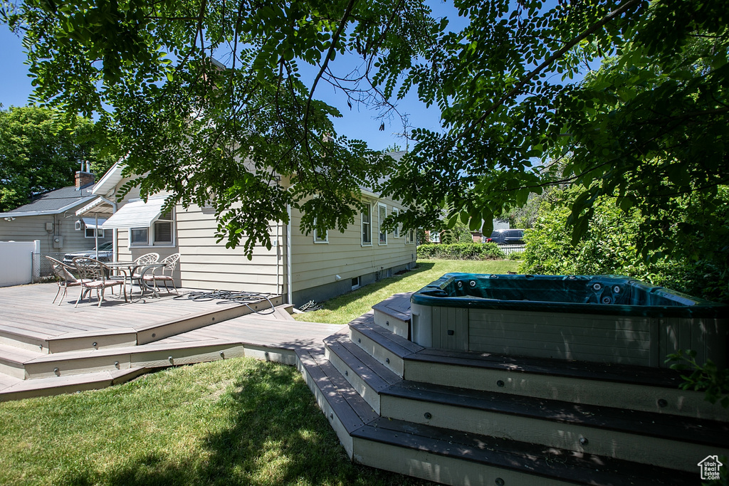 Wooden terrace featuring a hot tub, outdoor dining space, and a lawn