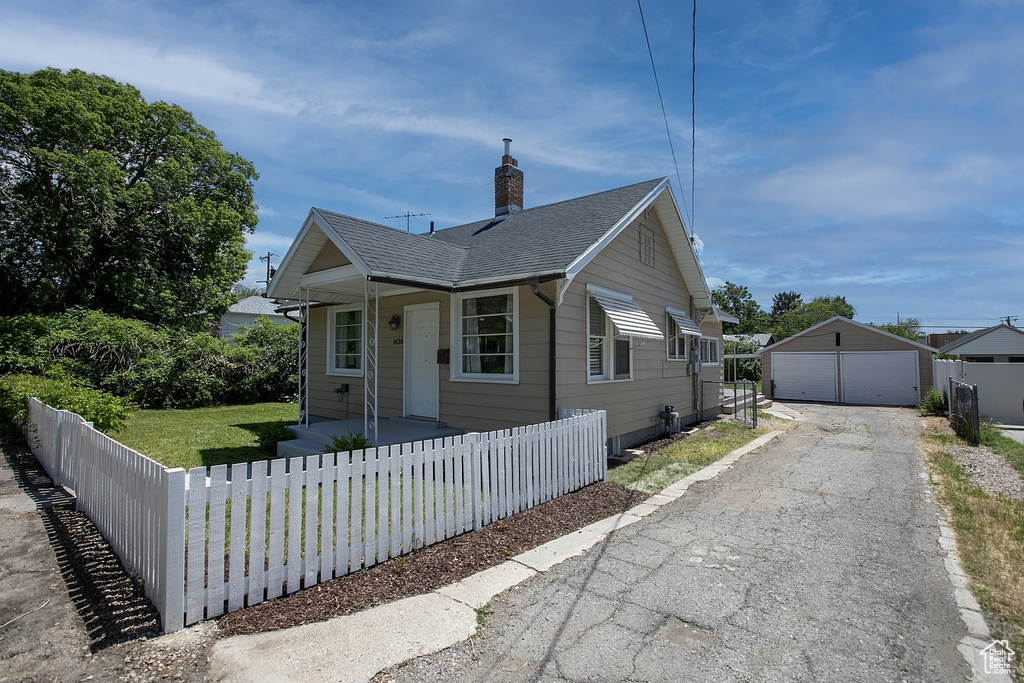 Bungalow with a detached garage, an outdoor structure, a chimney, a porch, and a shingled roof