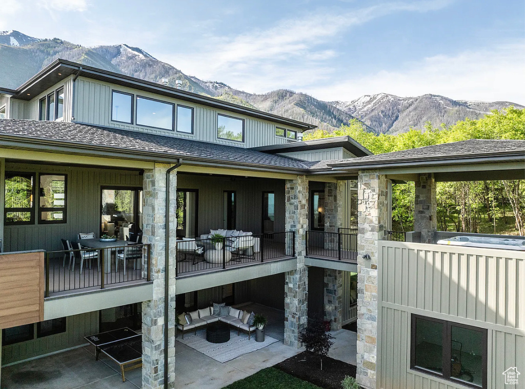 Rear view of house with a mountain view, an outdoor hangout area, stone siding, and a shingled roof