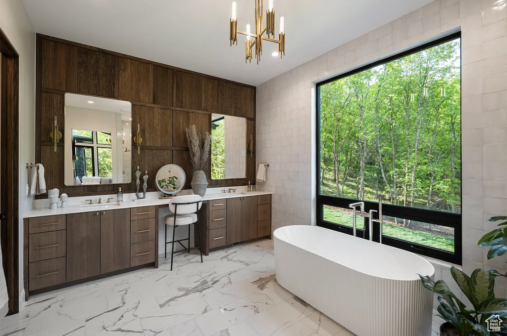 Bathroom with two vanities, a freestanding tub, marble finish flooring, tile walls, and a chandelier