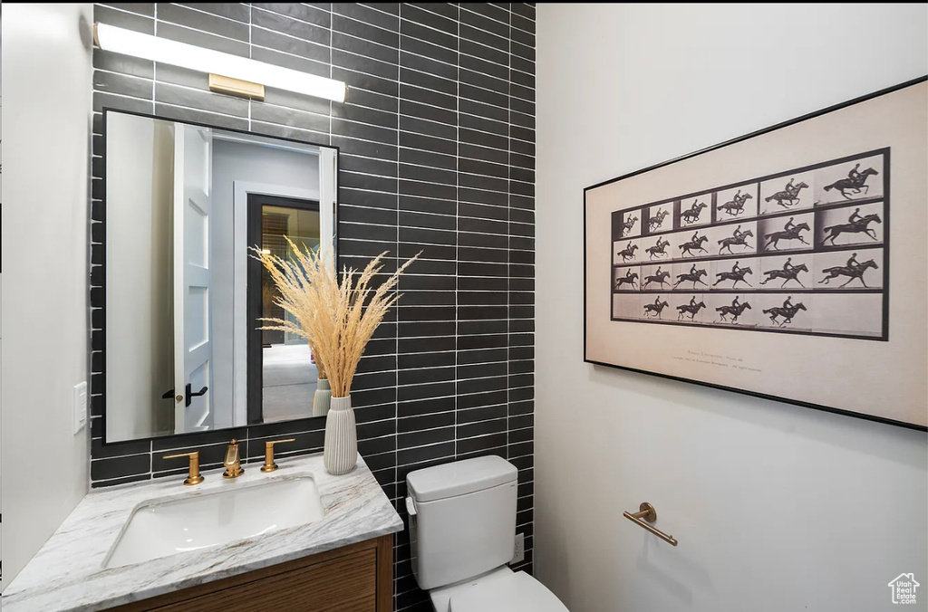 Bathroom featuring tile walls, vanity, toilet, and tasteful backsplash