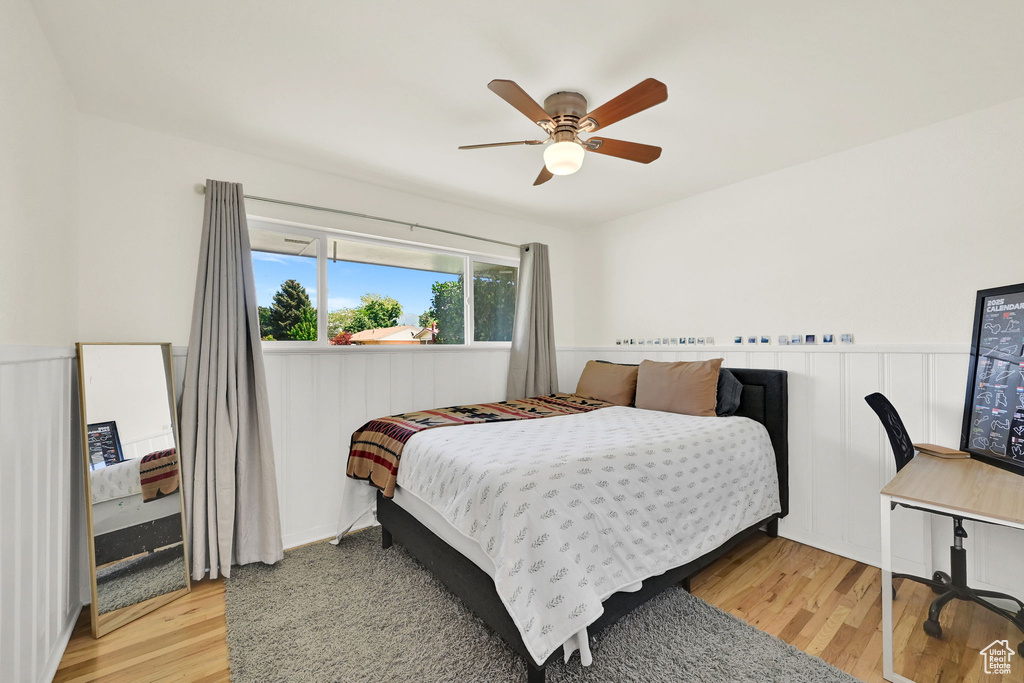 Bedroom featuring wood finished floors, a wainscoted wall, and a ceiling fan