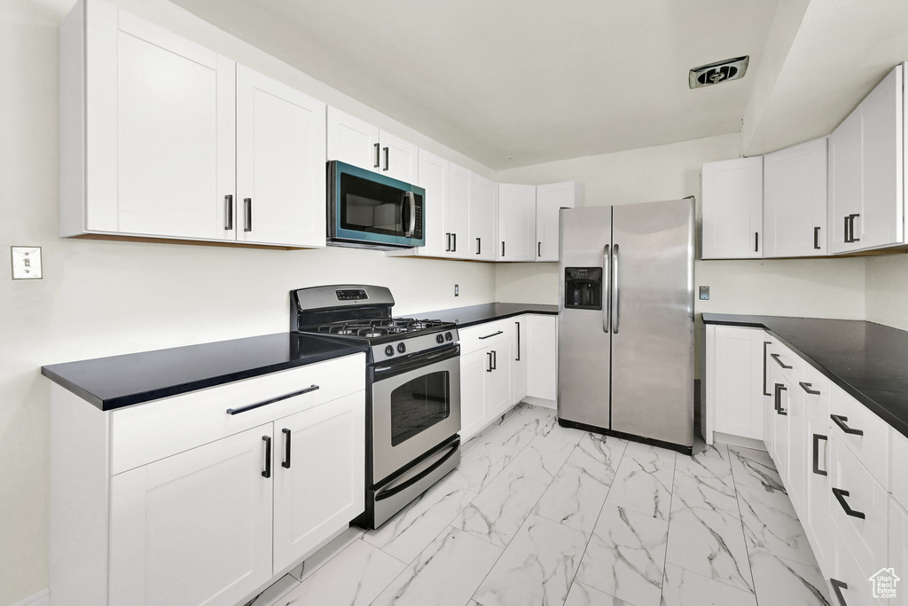Kitchen with stainless steel appliances, light marble finish floors, dark countertops, and white cabinetry