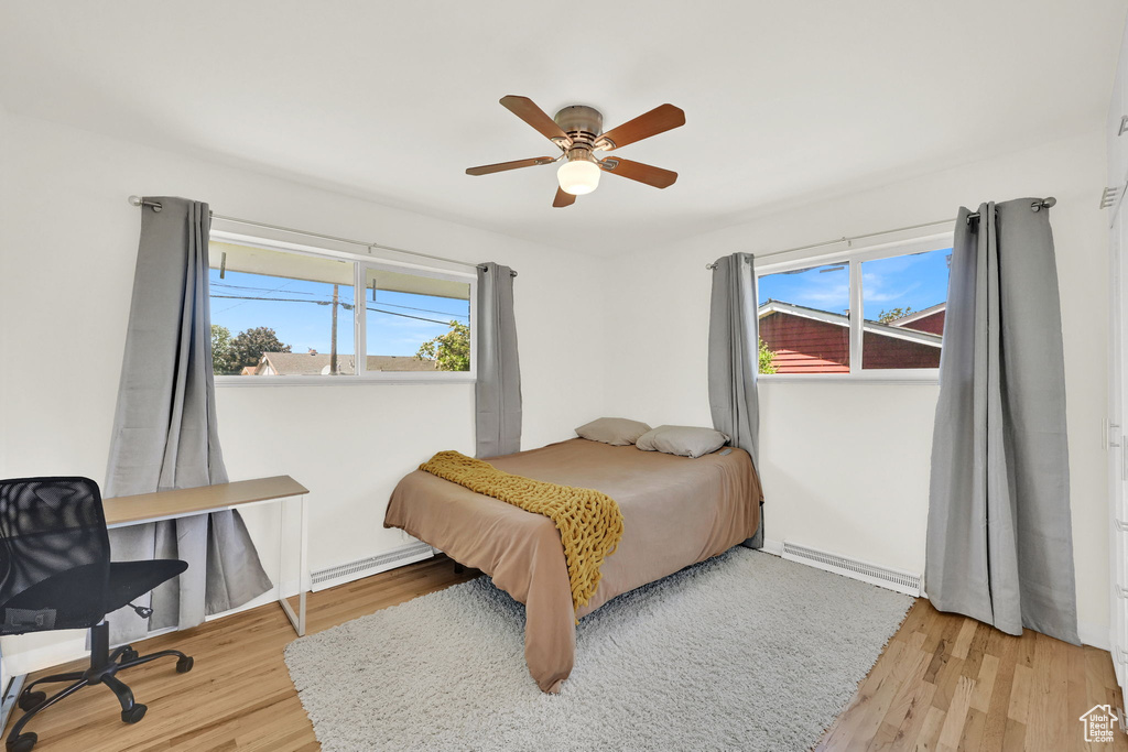 Bedroom with a baseboard radiator, light wood-type flooring, a ceiling fan, and a desk