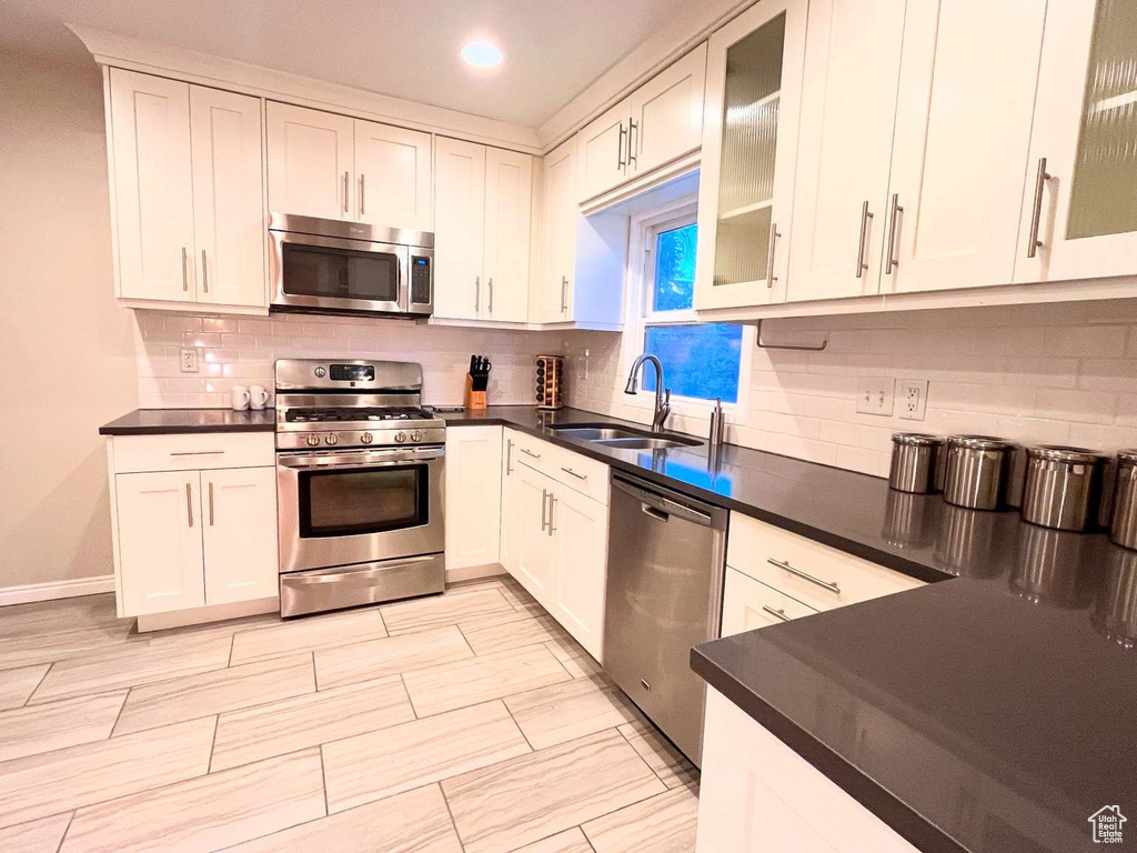 Kitchen featuring stainless steel appliances, a sink, dark countertops, recessed lighting, and backsplash