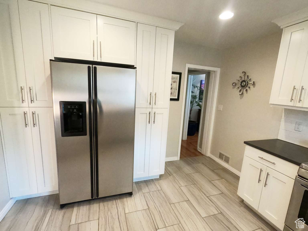 Kitchen featuring stainless steel fridge, baseboards, white cabinetry, light wood-type flooring, and dark countertops