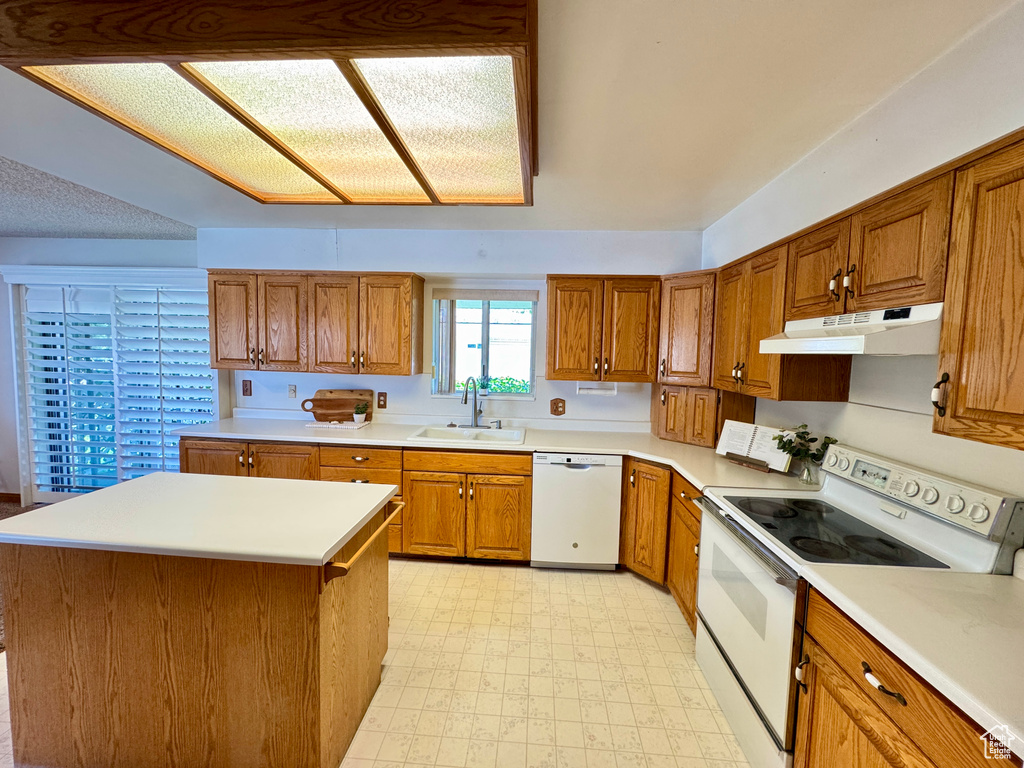 Kitchen featuring white appliances, under cabinet range hood, a sink, light flooring, and brown cabinetry