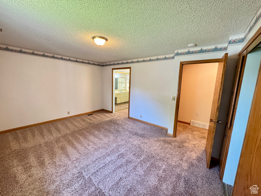 Carpeted empty room featuring a textured ceiling and baseboards