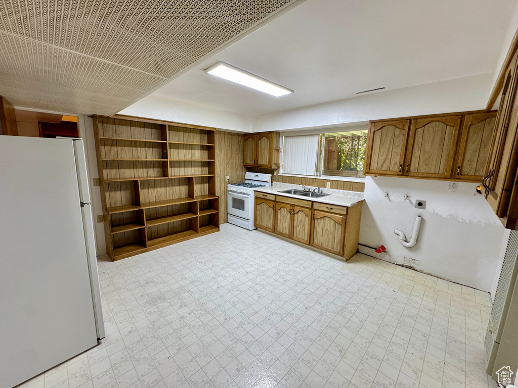 Kitchen with white appliances, a sink, brown cabinetry, light countertops, and light floors