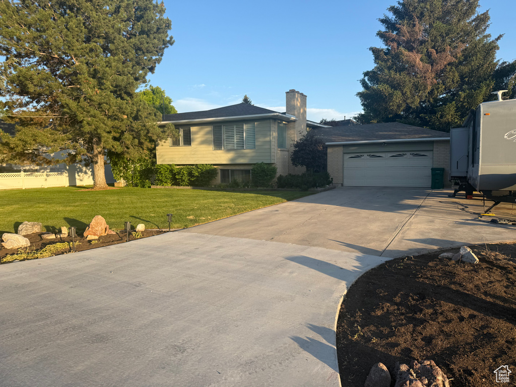 Split level home with a chimney, a garage, concrete driveway, and a front yard