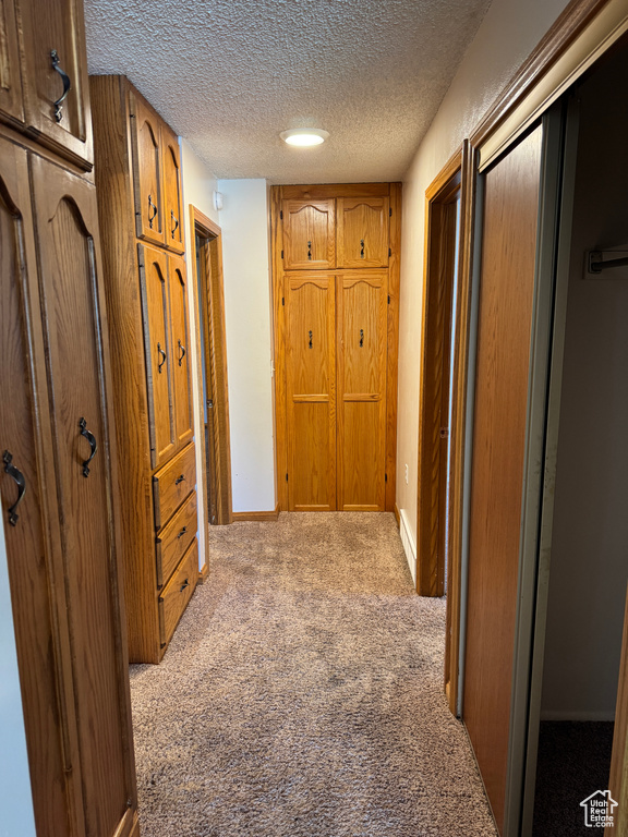 Hall with carpet flooring, a textured ceiling, and baseboards
