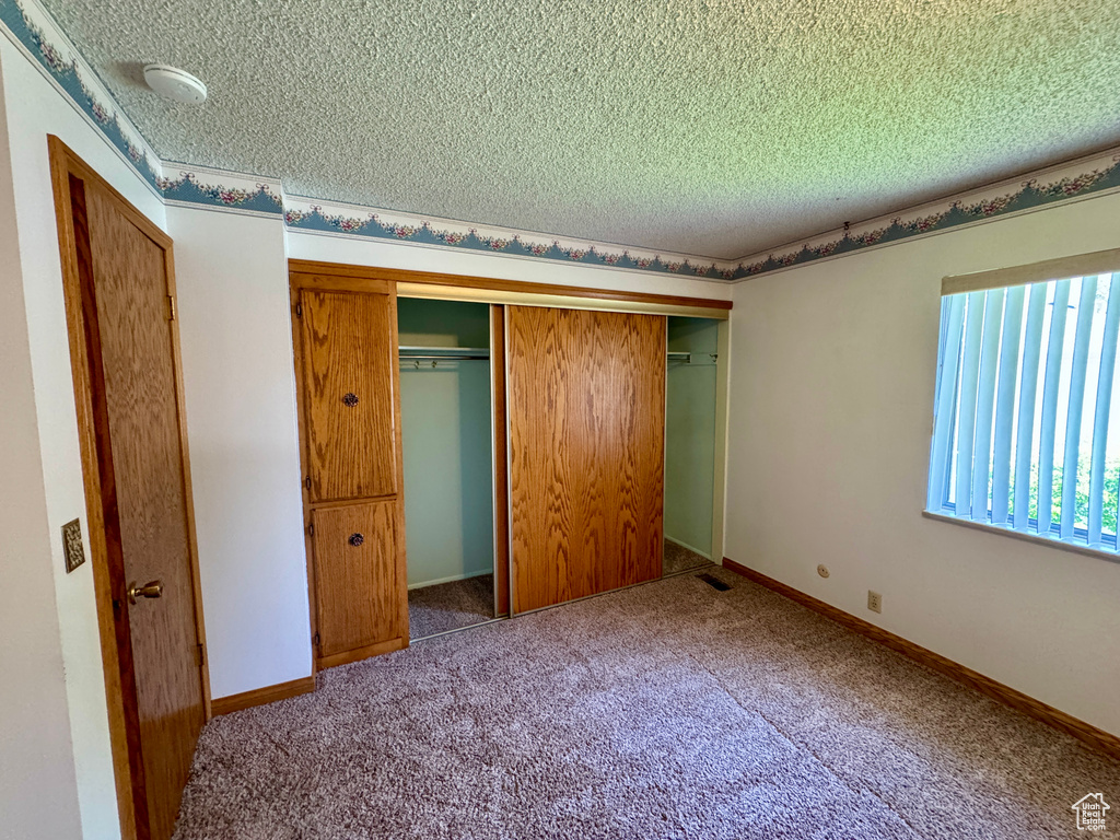 Unfurnished bedroom with a textured ceiling, a closet, and carpet flooring