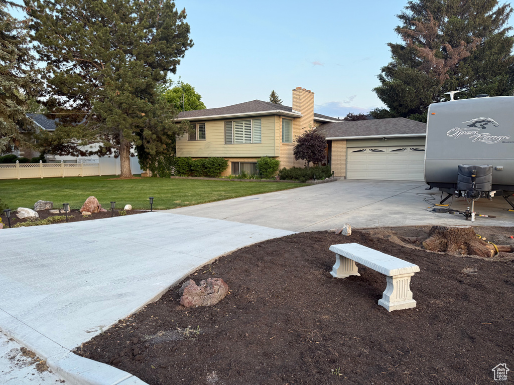 Split level home with concrete driveway, a garage, a chimney, and brick siding