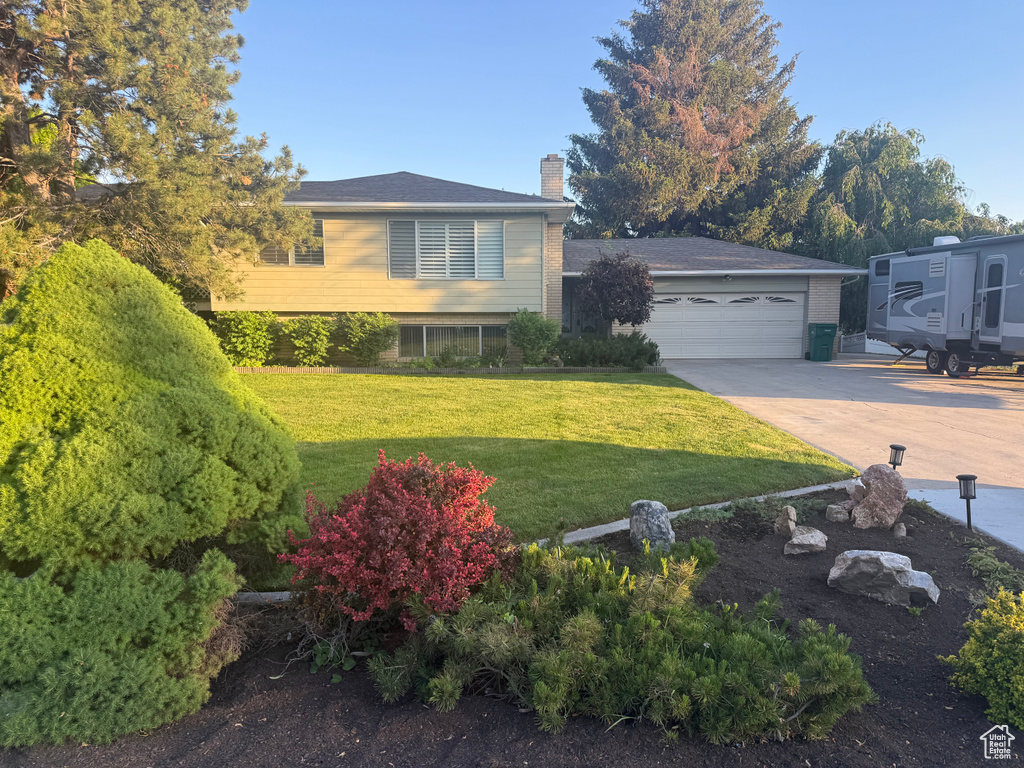 Split level home featuring a chimney, a garage, driveway, a front lawn, and brick siding