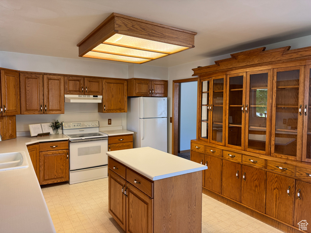 Kitchen with white appliances, under cabinet range hood, light flooring, and brown cabinets