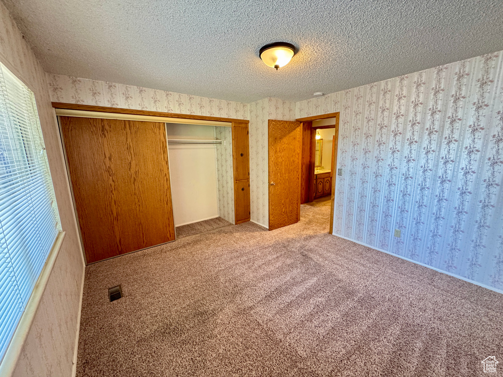 Unfurnished bedroom with wallpapered walls, a closet, carpet floors, and a textured ceiling