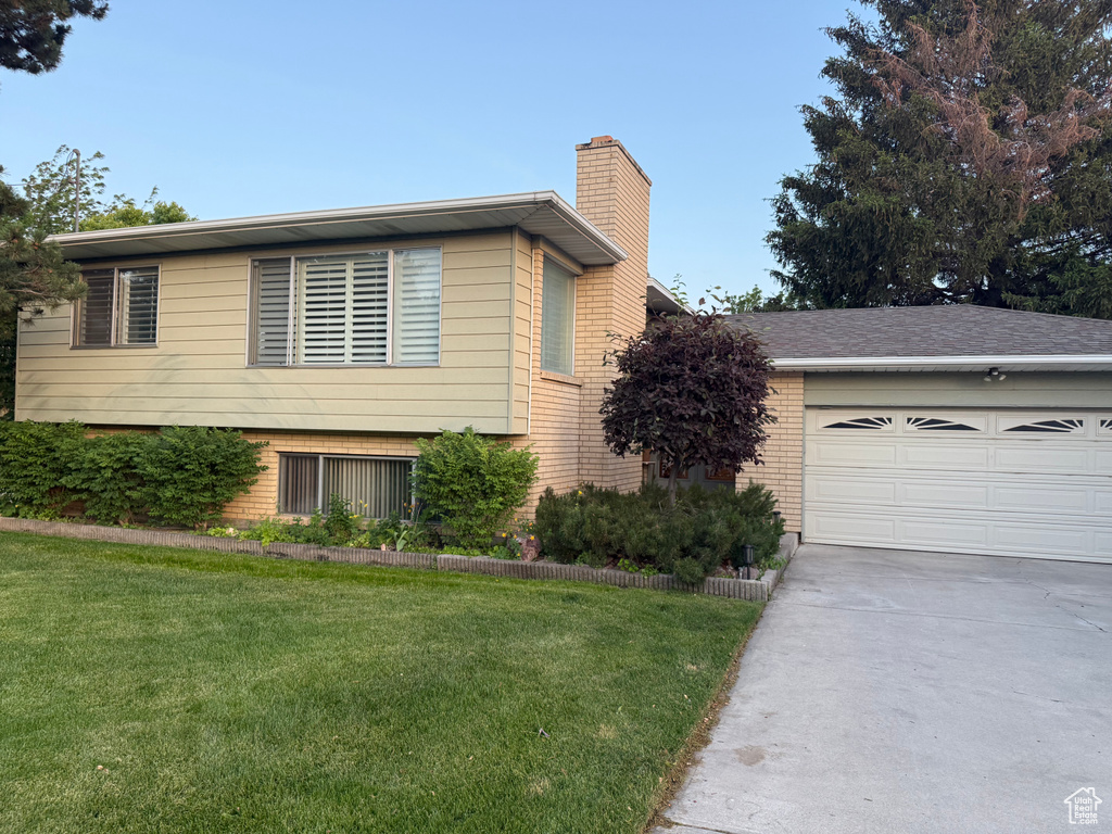 Tri-level home featuring a chimney, brick siding, concrete driveway, and a front yard
