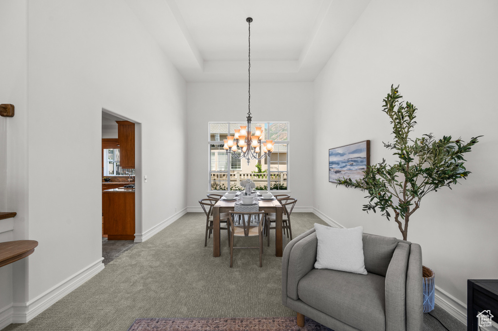 Carpeted dining room with a chandelier, a high ceiling, a tray ceiling, and baseboards