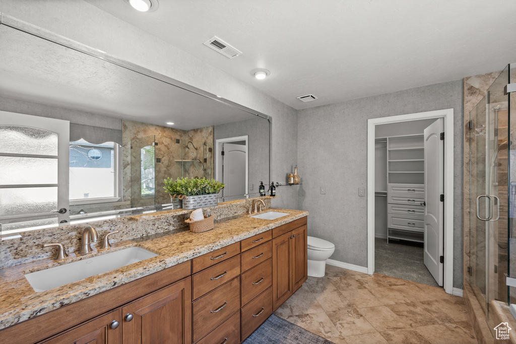 Bathroom with double vanity, a stall shower, toilet, a spacious closet, and baseboards