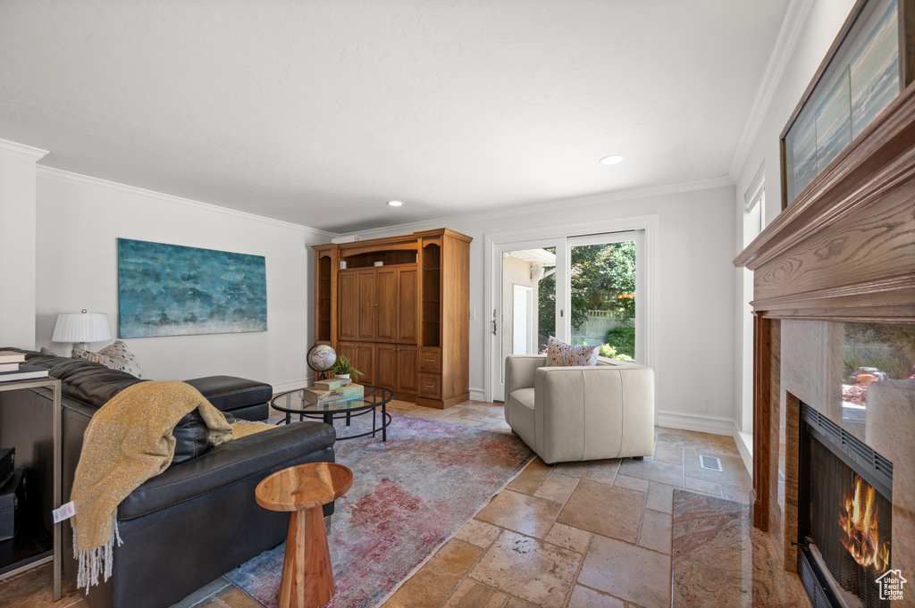 Living room with a fireplace, stone tile flooring, crown molding, recessed lighting, and baseboards
