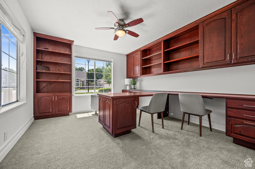 Office space with built in study area, ceiling fan, light colored carpet, and baseboards